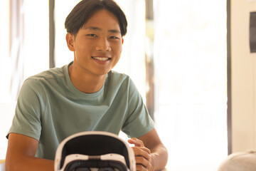 Smiling teenage boy sitting at desk with VR headset in high school classroom