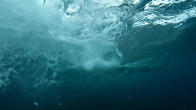 Turbulent underwater scene during a storm. Chaotic currents swirl beneath massive waves. Dark, foreboding atmosphere contrasts with eerie calm of the depths. Whitecaps and spray visible from below. 
