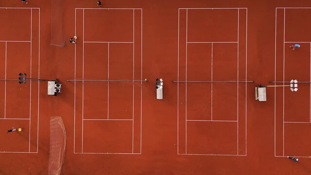 People practicing tennis on clay courts. The aerial camera moves horizontally over the courts