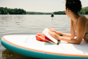 young woman reading. book on paddle board 