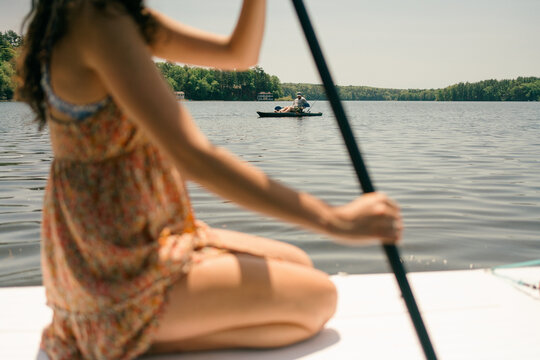 young woman  kneeling on her paddle board and heading out on the lake 