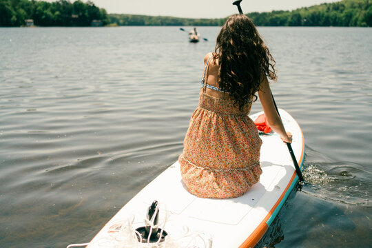 young woman  kneeling on her paddle board and heading out on the lake 