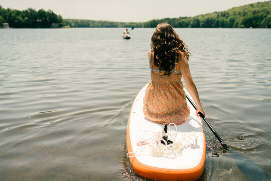 young woman  kneeling on her paddle board and heading out on the lake 