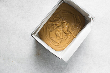 Overhead view of peanut butter fudge poured into a lined baking tin, top view of soft peanut butter fudge in a parchment lined baking pan, process of making peanut butter fudge