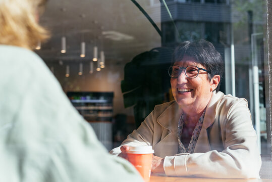 Hopeful Adult Woman laughing through a window while drinking coffee