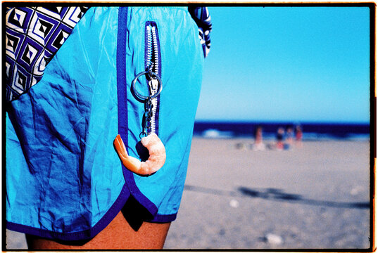 man wearing a shrimp-shaped key chain on the beach, 35mm film