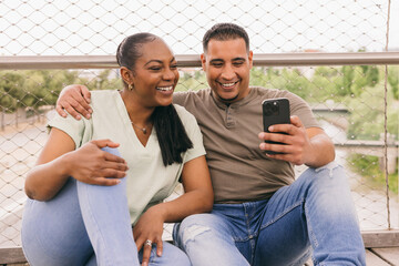 Curvy Dominican couple enjoying time on a bench with a smartphone