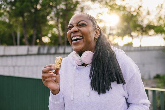 Curvy Dominican woman enjoying a snack outdoors with laughter