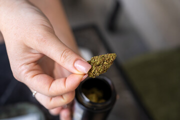 Young Woman Holding Cannabis Bud Above Jar.