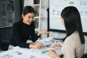 Fototapeta premium Two Businesswomen Analyzing Financial Data and Charts in a Modern Office Setting