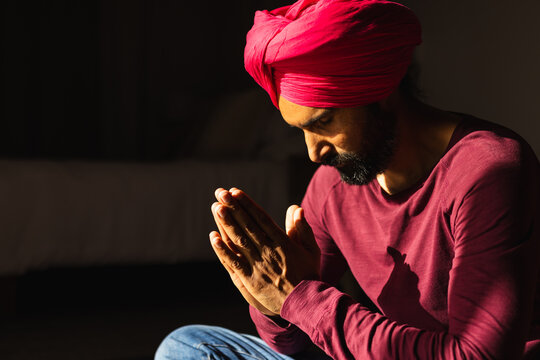 Praying, man in red turban and shirt sitting with hands together