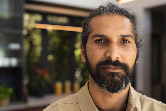 Portrait of man with beard and long hair looking at camera indoors