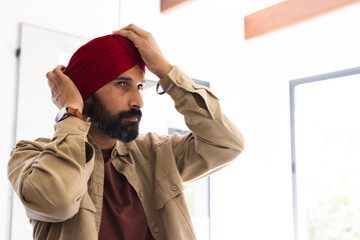 Adjusting red turban, man standing indoors, focusing on traditional attire, copy space