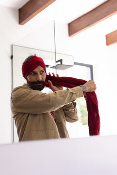 Tying red turban, man standing in front of mirror at home