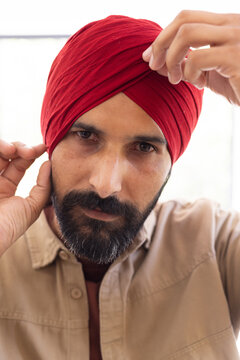 Adjusting red turban, man focusing on traditional headwear at home