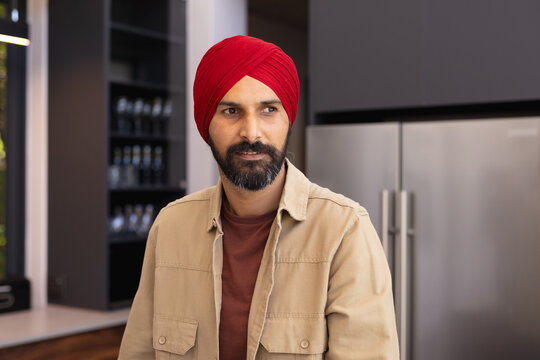 Man in red turban standing in modern kitchen, looking thoughtful - Powered by Adobe