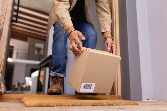 Receiving package delivery, man picking up cardboard box from doorstep