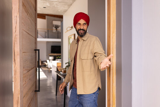Welcoming guests, man in turban opening door and inviting inside home