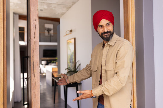 Welcoming guests, man in red turban inviting into modern home interior