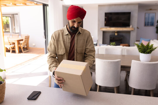 Man in turban opening package in modern home, smartphone on counter