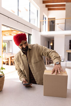 Receiving package, man in turban holding smartphone and touching cardboard box