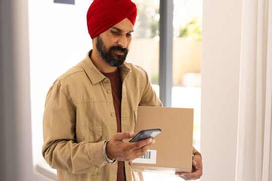Holding package, man scanning barcode with smartphone at home