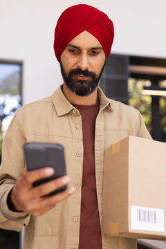 Holding smartphone, man with package checking delivery details at home