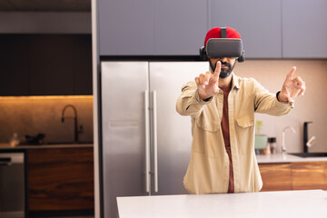 Using VR headset, man interacting with virtual environment in modern kitchen, copy space