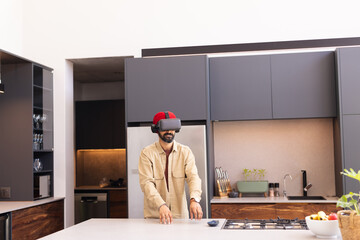 Using VR headset, man exploring virtual reality in modern kitchen at home, copy space