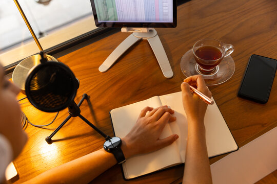 Recording podcast young woman writes in notebook at desk with tablet and microphone