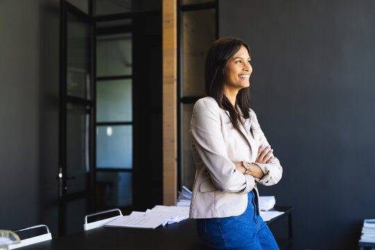 Standing confidently in office, businesswoman smiling and looking away