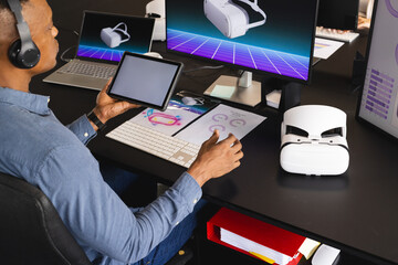 Using tablet and VR headset, man working on virtual reality project in office