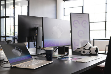 On office desk, laptop, VR headset, and technology design charts in modern workspace