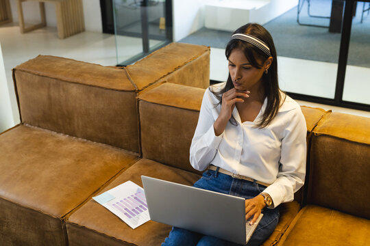 Working on laptop, woman analyzing business reports while sitting on couch, copy space