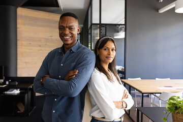 Standing back-to-back in modern office, business professionals smiling confidently