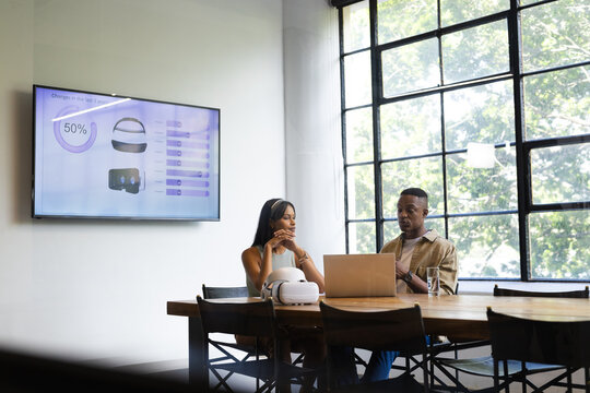 Discussing virtual reality technology, business colleagues using laptop and presentation screen in o