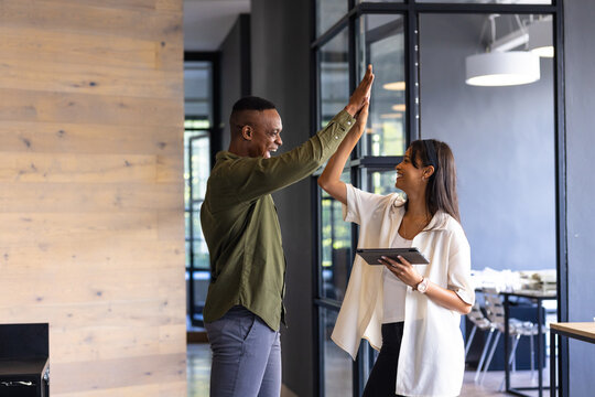 Celebrating success in office, colleagues high-fiving while holding tablet, copy space