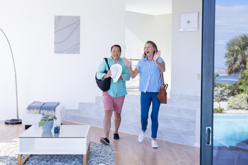 Entering vacation home, senior couple excitedly arriving with bags and hats