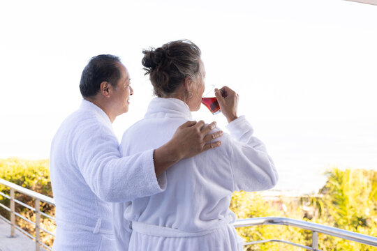 Senior couple in bathrobes enjoying morning drink on balcony with ocean view - Powered by Adobe