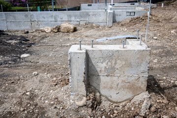 Beginnings of new residential home construction, dirt lot with cement foundation retaining walls and support pylons, as a building development background
