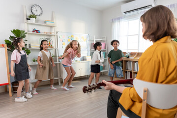 Caucasian young woman teacher playing guitar with students in school.