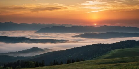 Fototapeta premium A beautiful sunrise casts an orange glow over a mountain range, with layers of fog rolling through the valleys