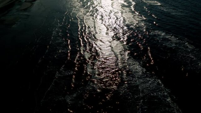 Dark black water with a mysterious wave pattern and light reflections creates an enigmatic and captivating scene, highlighting the sea's natural beauty.