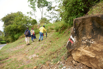 Obraz premium A group of three unrecognizable people enjoy the outdoors hiking, walking along a rural trek between Barichara and Guane, in Colombia. Color arrows painted on a rock show the correct way to the hikers