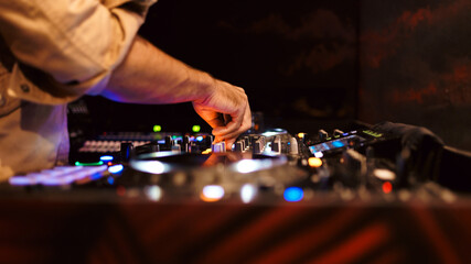 Close up DJ plays live set and mixing music on turntable console in the night club. Disc Jokey Hands on a sound mixer station at club party. DJ mixer controller panel for playing music and partying.