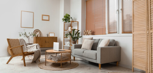 Interior of modern living room with grey sofa, armchair and laptop on coffee table