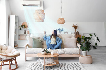 Young woman switching on air conditioner in living room