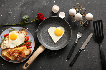 Composition with tasty fried eggs, cut croissant, tomatoes in plate and rose flower on dark background