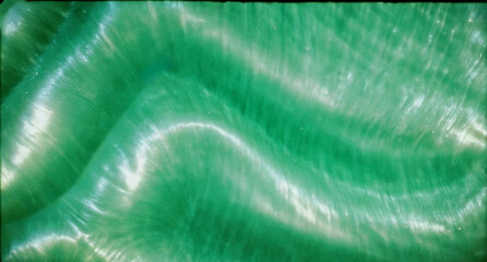 close-up of green, wavy texture, silk fabric, liquid with light reflections, summer green background