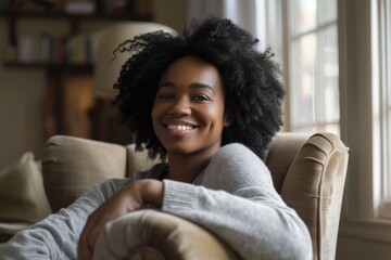 Fototapeta premium A young African American woman sits comfortably in a chair and smiles warmly.